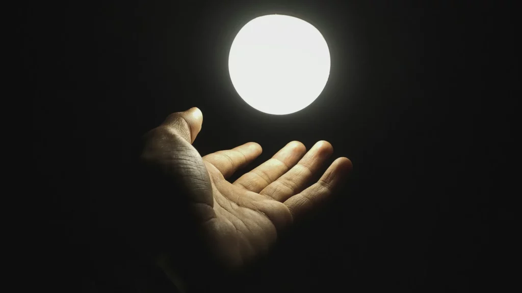 Dłoń wyciągnięta w ciemności trzymająca jasne światło – metafora odkrywania potencjału i świadomej pracy z talenty Gallupa (Gallup's top 5 talents).